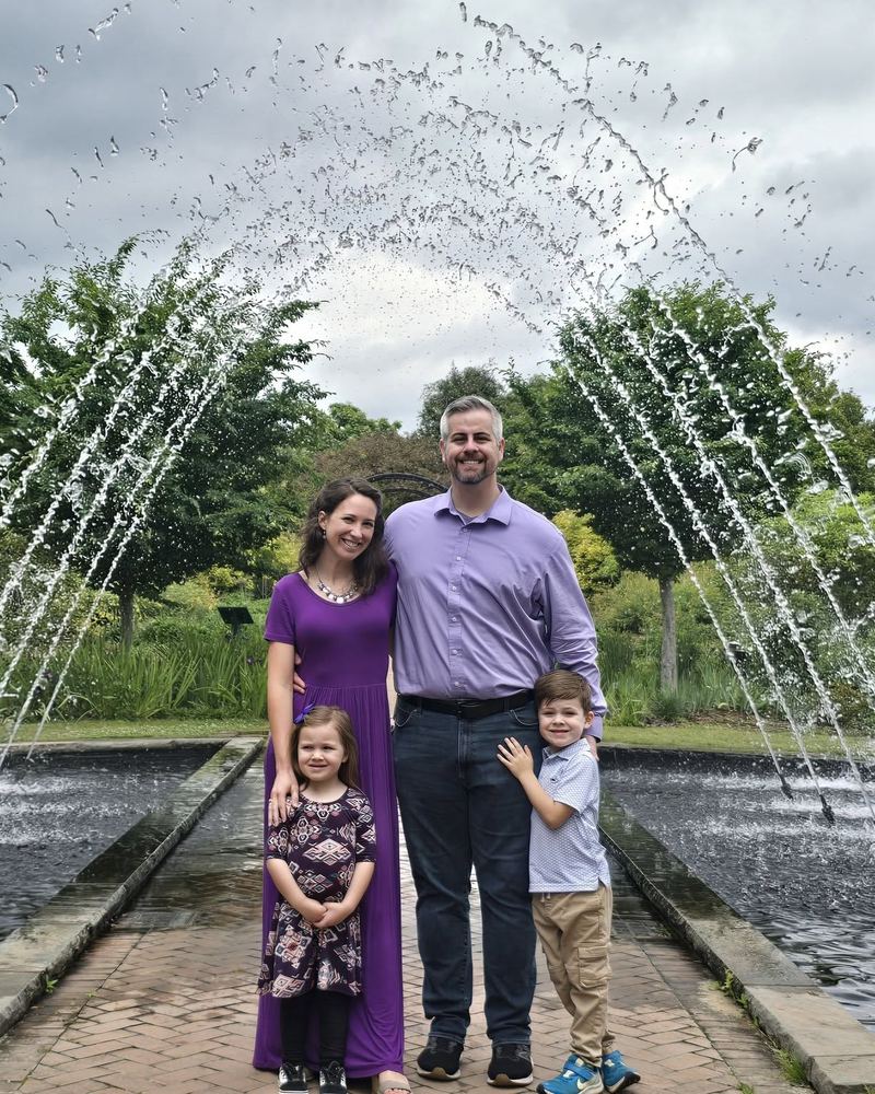 Matthew and Rachel Carpenter with their two children, standing beneath a garden fountain